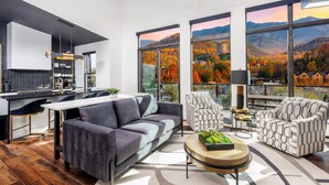 A modern living space with a kitchen, seating area, and large windows offering a view of autumn foliage and mountains. - 5min walk to Gatlinburg|Mtn View|Sauna|Indr Pool|Game| (Gatlinburg)