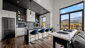 A modern kitchen with a central island, bar stools, and a large window offering a city view. - 5min walk to Gatlinburg|Mtn View|Sauna|Indr Pool|Game| (Gatlinburg)