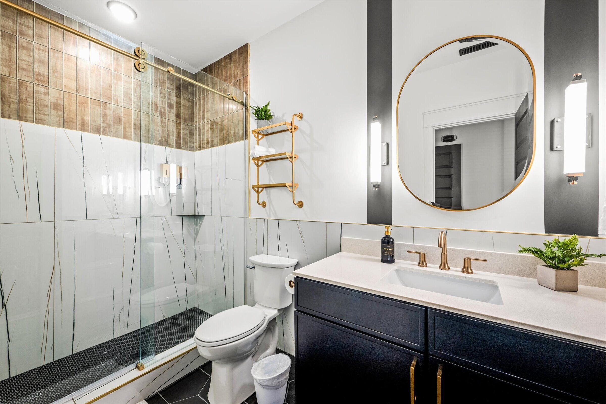 Une salle de bain moderne avec une douche à l’italienne en verre, des toilettes, un lavabo avec un miroir et une petite plante posée sur le comptoir.