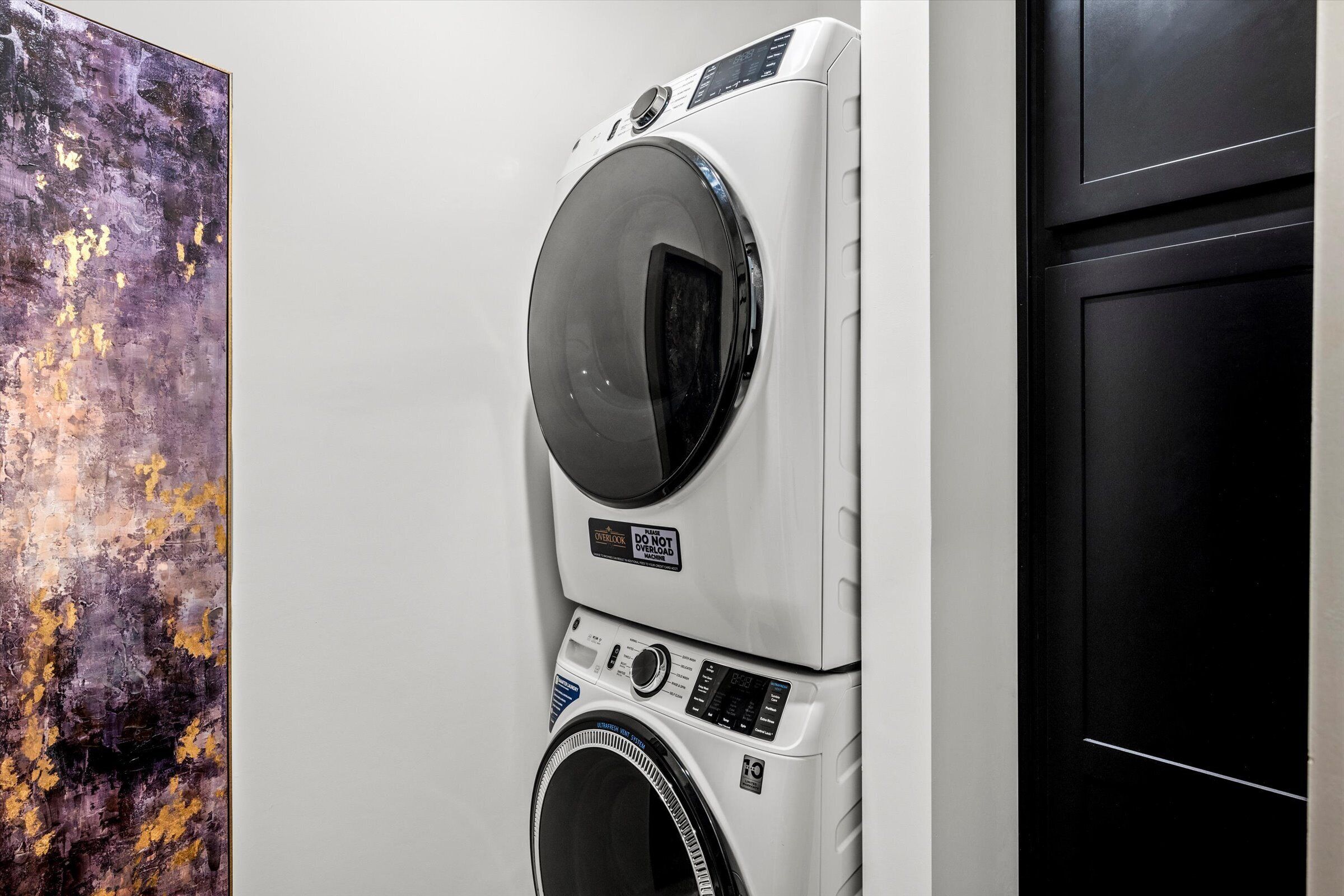 A stacked washer and dryer unit in a room with a plain wall and a door.