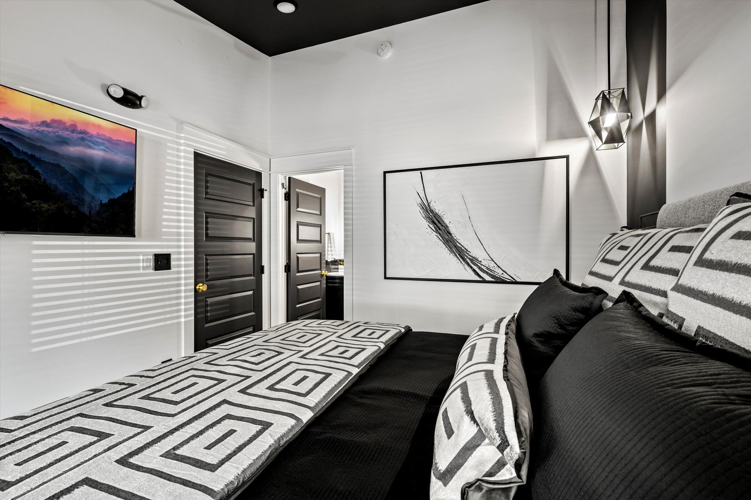 A modern bedroom with a bed, a painting, and a geometric-patterned blanket.