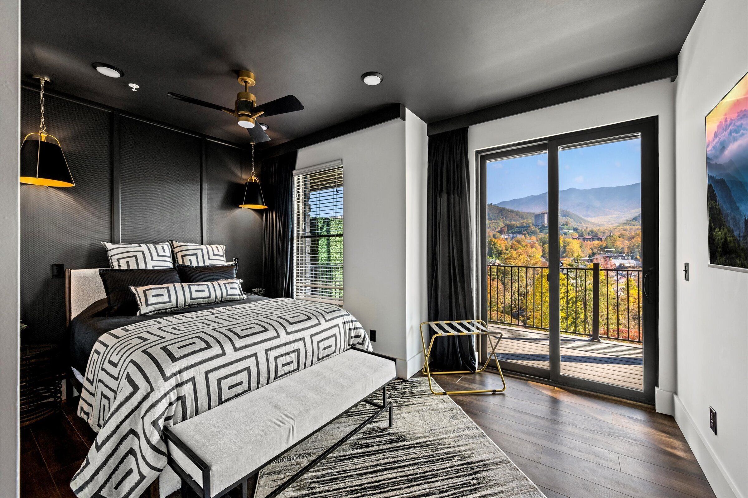 A modern bedroom with a large bed, a ceiling fan, and a view of a scenic landscape through a sliding glass door.