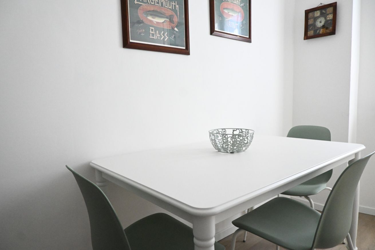 A dining area with a white table, two green chairs, and a decorative metal bowl.
