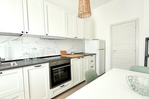 Uma cozinha moderna com armários brancos, forno preto, painel de parede em mármore e uma mesa de jantar com cadeiras.