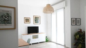 A modern living room with a flat-screen TV on a white cabinet, a wicker pendant light, and a sliding glass door leading to a balcony. - SE163 – Senigallia, new one-bedroom apartment with balcony in the town center (Senigallia)