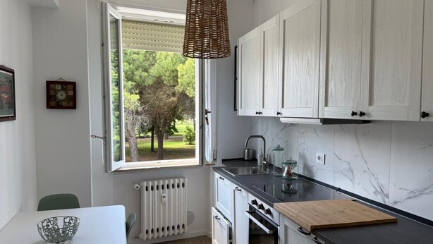 A kitchen with white cabinets, a black countertop, a window with a view of greenery, and a hanging light fixture. - SE163 – Senigallia, new one-bedroom apartment with balcony in the town center (Senigallia)