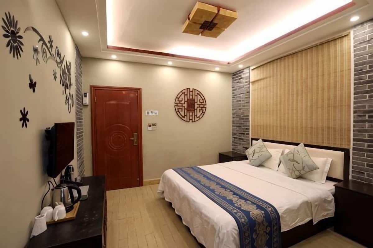 A bedroom with a bed, a bedside table, a wall-mounted TV, a door, and a decorative wall piece.