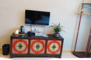 Um armário de madeira com painéis decorativos, uma televisão de tela plana montada acima, uma cafeteira, uma planta e um cabideiro.