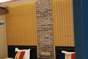 Quarto de hotel com parede de destaque em tijolo, uma cama com cabeceira e uma janela com persianas.