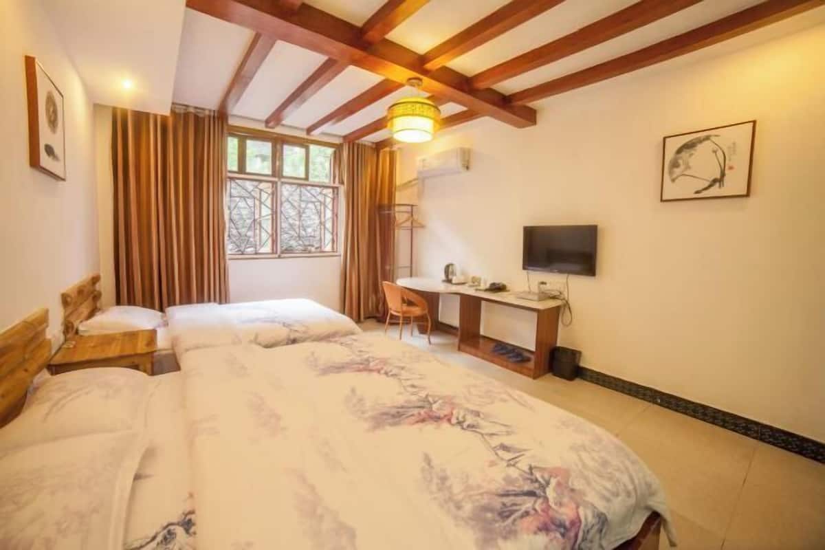 A bedroom with a bed, a desk, a chair, a TV, and a window with curtains.