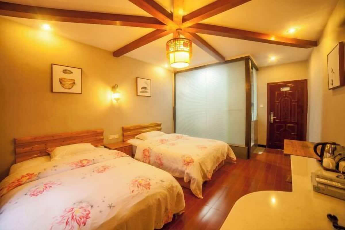 A room with two beds, wooden beams on the ceiling, a chandelier, and a door.