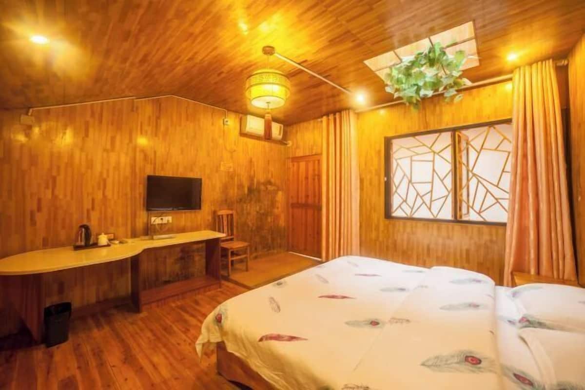 A wooden-themed room with a bed, desk, and TV.