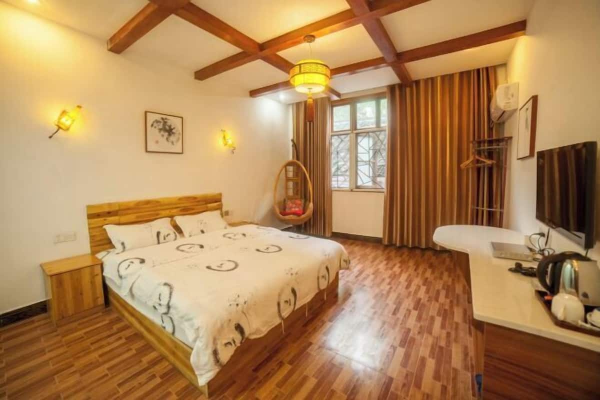 A bedroom with a wooden bed, a bedside table, a hanging chair, a window with curtains, and a desk with a chair.