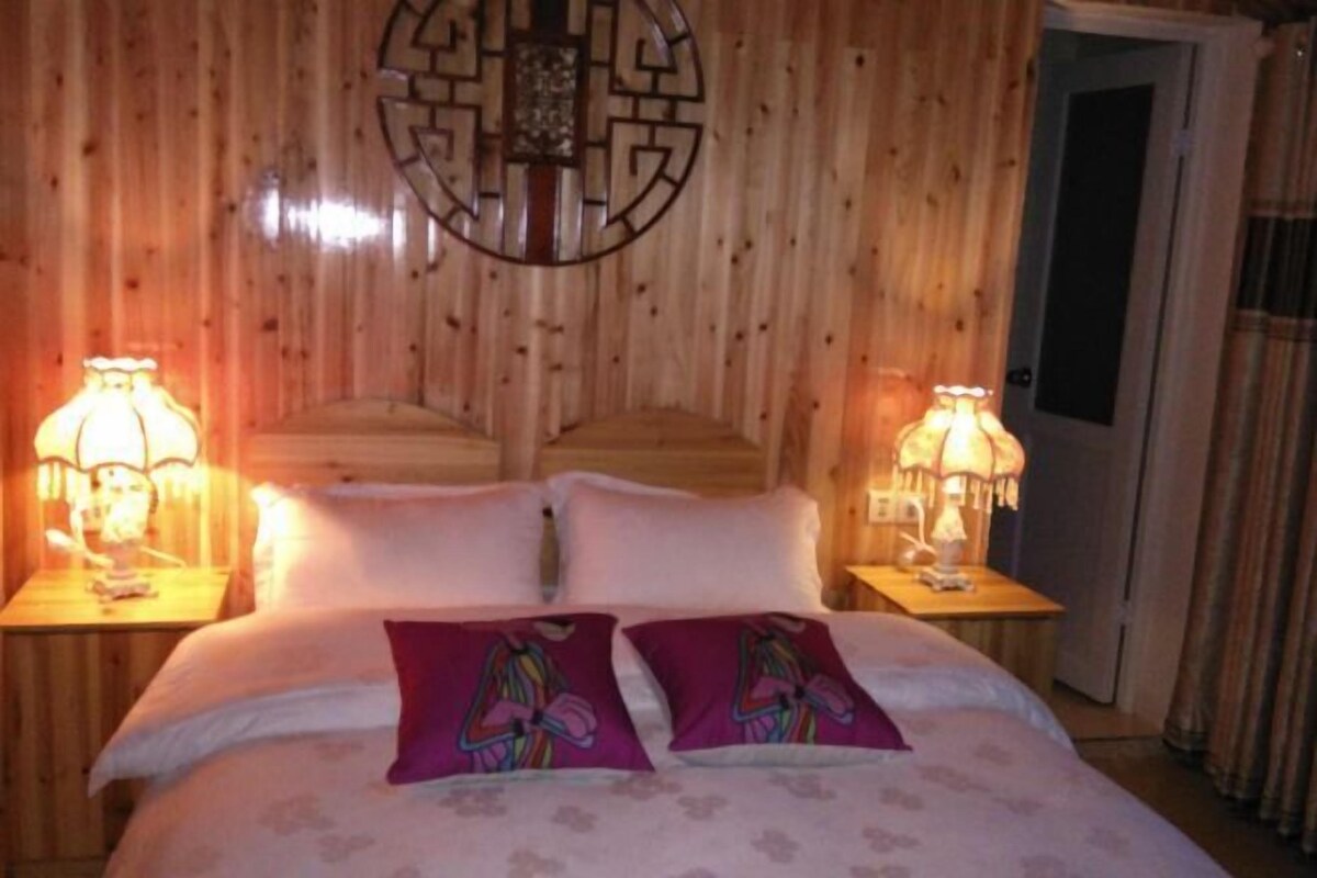 Quarto com painéis de madeira, uma cama, duas mesas de cabeceira e um objeto decorativo na parede.