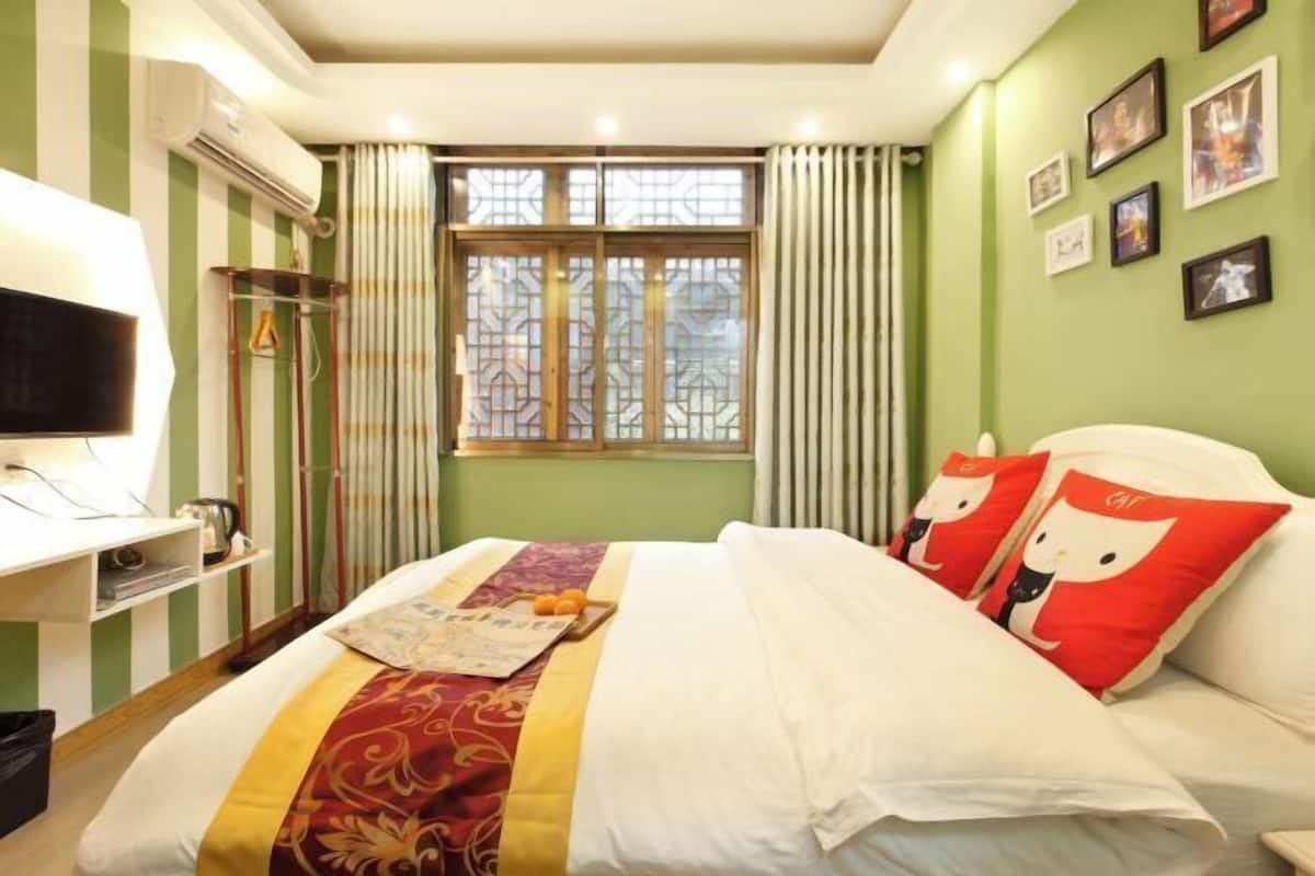 A hotel room with a bed, a television, a window with curtains, and a wall with framed pictures.