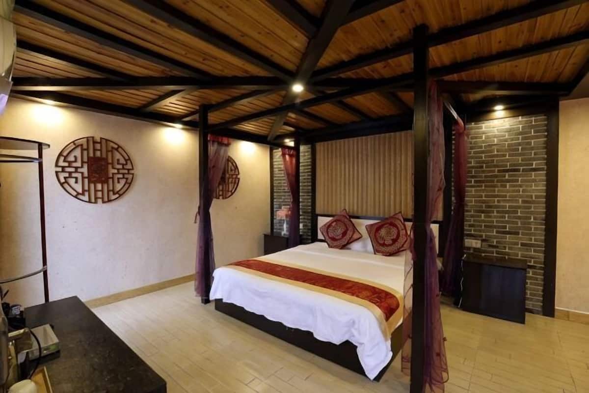 A bedroom with a wooden ceiling, a bed with a white and red bedspread, and a brick wall.