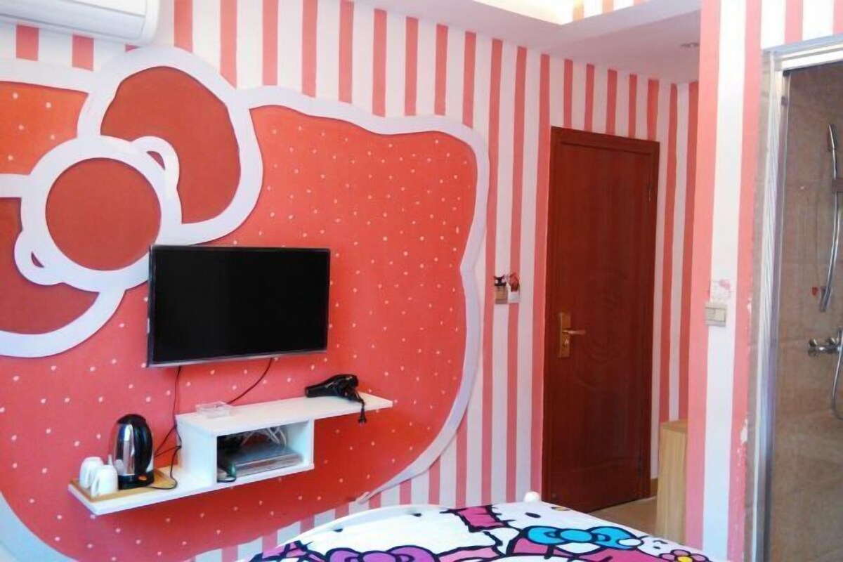 Quarto com parede listrada, televisão montada, cama com colcha colorida e área de chuveiro.