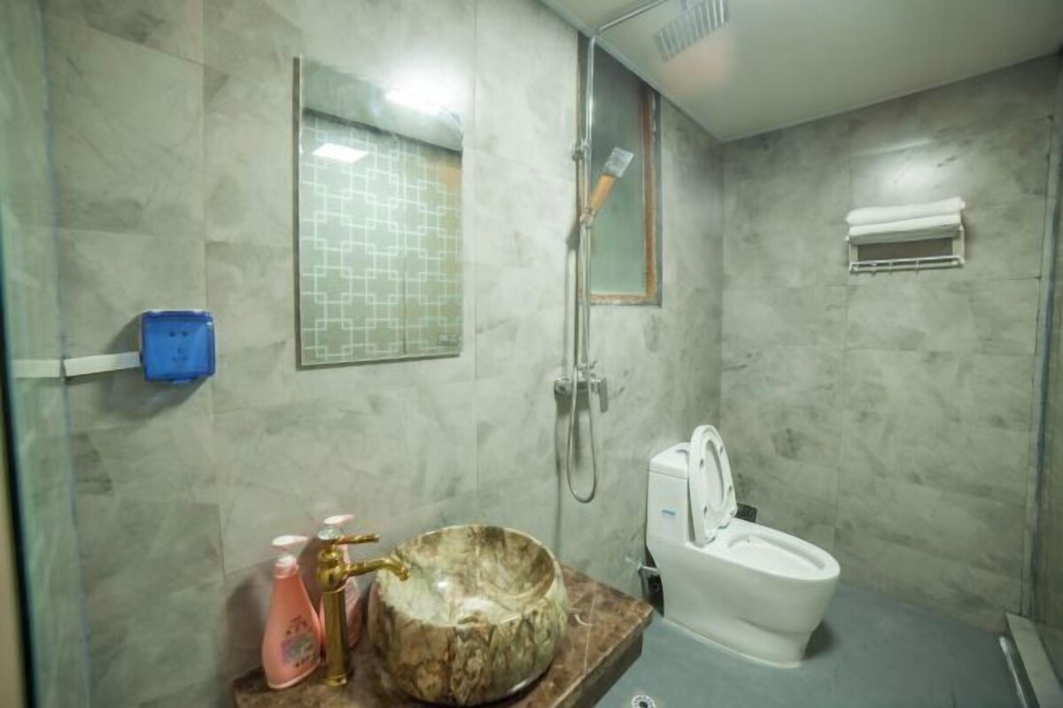 Casa de banho com lavatório de mármore, chuveiro manual, sanita e barra para toalhas.