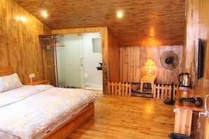 Quarto com painéis de madeira, uma cama, uma mesinha com abajur e um ventilador.