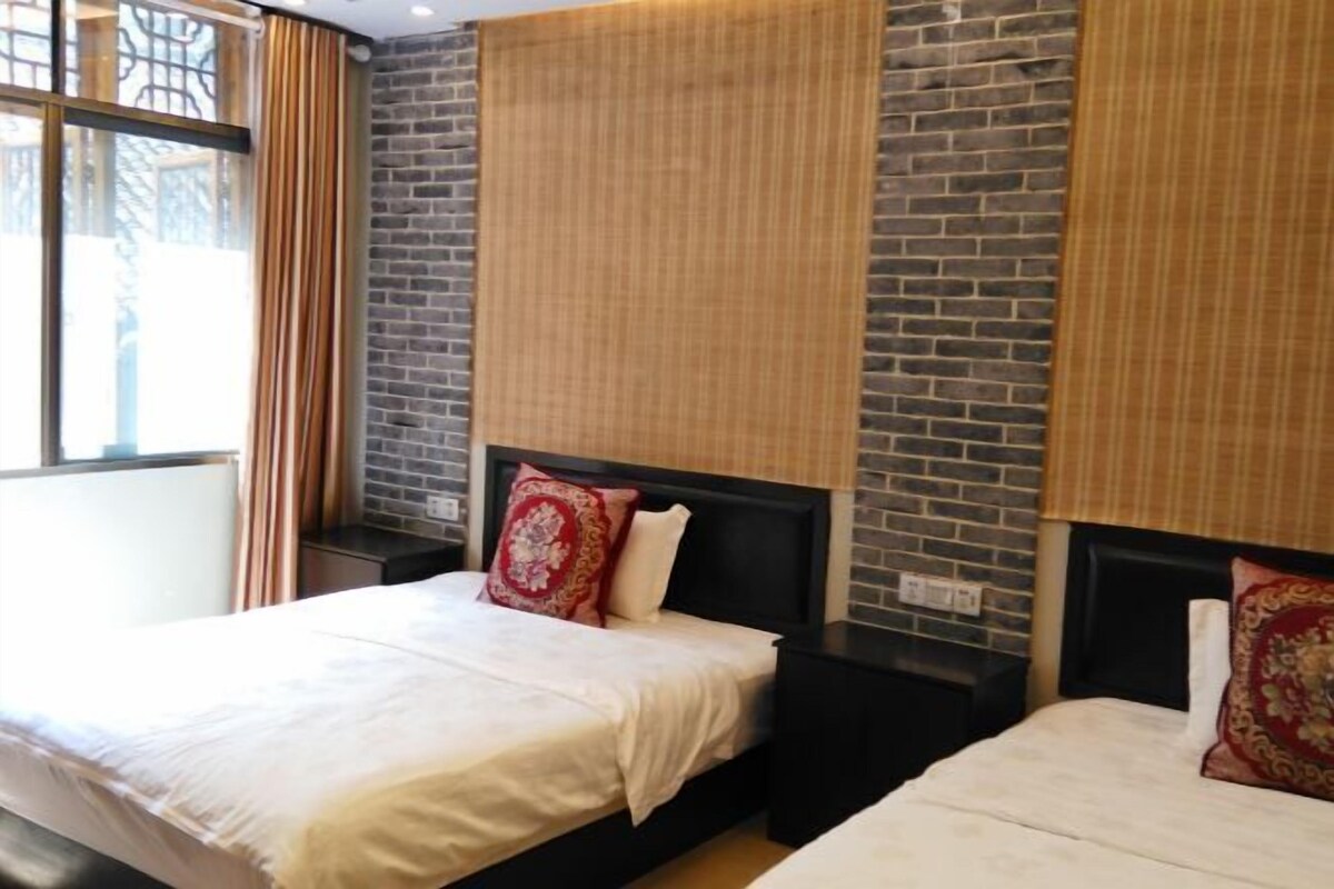 Quarto de hotel com duas camas, parede de tijolos e janela com cortinas.
