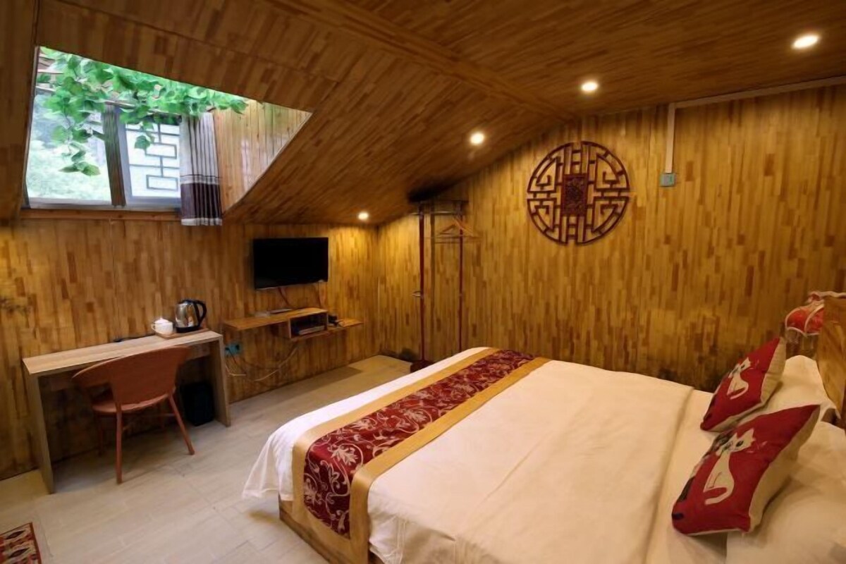 Quarto de madeira com cama, escrivaninha e televisão.