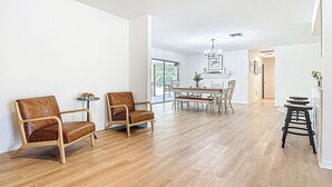 Una habitación amplia con suelo de madera, dos sillones de cuero, una mesa de comedor con sillas, un ventilador de techo y una araña.