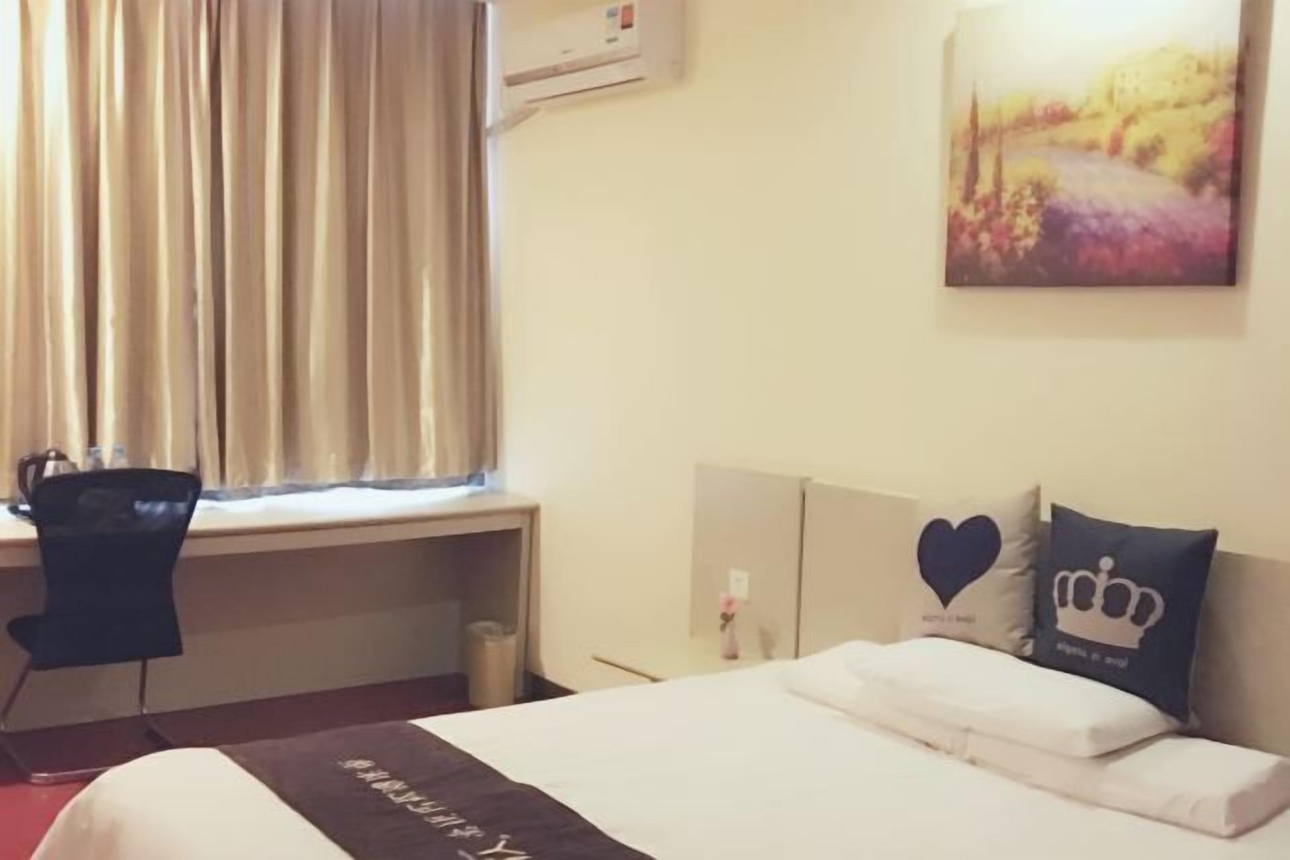 A hotel room with a bed, a desk, a chair, a window with curtains, and a painting on the wall.