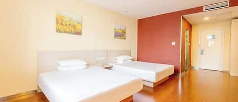 A hotel room with two beds, wooden flooring, and a door leading to another room.