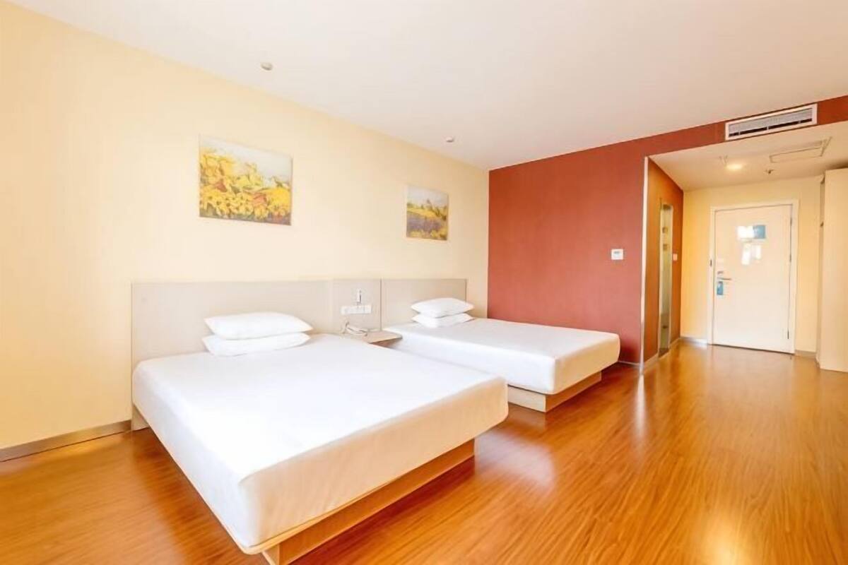 A hotel room with two beds, wooden flooring, and two wall-mounted paintings.