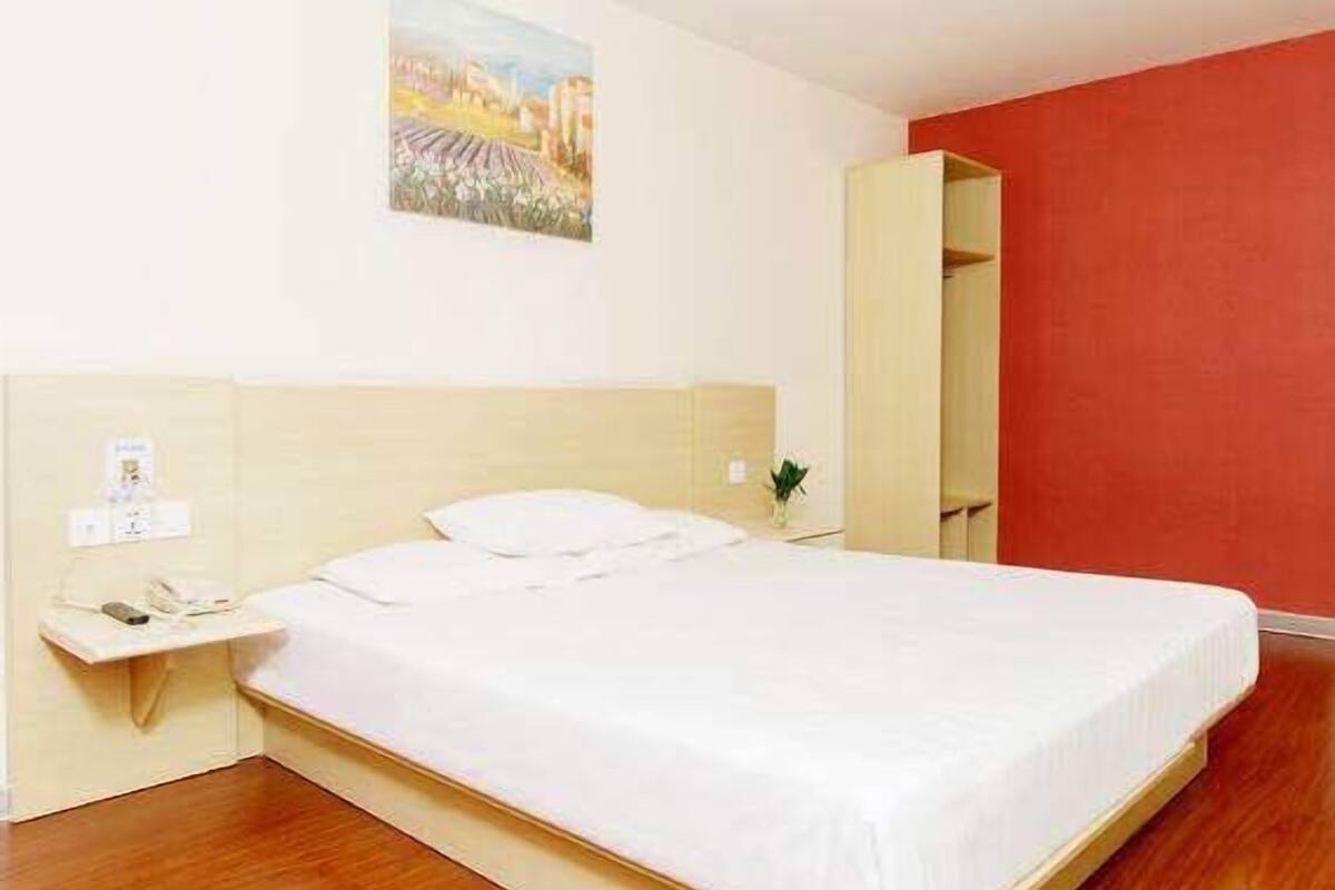 A hotel room with a bed, a bedside table, a nightstand, and a red accent wall.