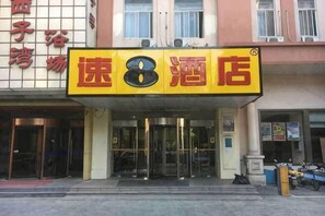 A hotel entrance with a prominent sign, glass doors, and a small parking area with a motorcycle.