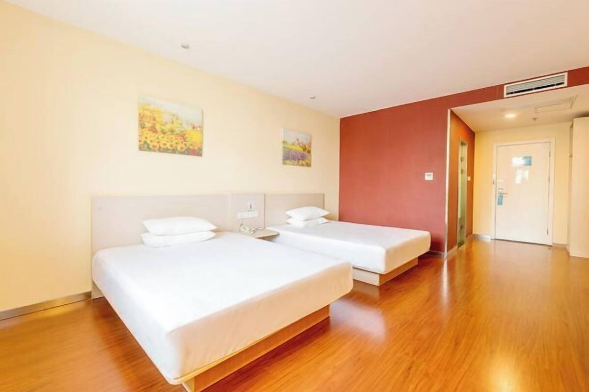 A hotel room with two beds, wooden flooring, and a door leading to a hallway.