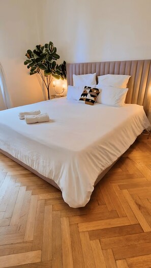 A neatly made bed with white linens and a geometric pillow, a bedside plant, and a wooden herringbone floor. - A jazzy and spacious apartment on the Promenade des Anglais (Nice)