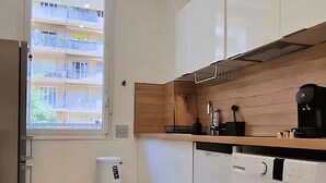 Een moderne keuken met witte kastjes, een inbouw wasmachine en een raam met uitzicht op een meer verdiepingen tellend gebouw.