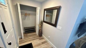 A hallway with a wooden floor, a bench, a mirror, and a door.
