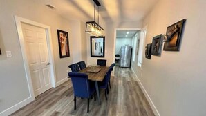 A dining area with a wooden table and blue chairs, a modern pendant light, and a refrigerator in the background.