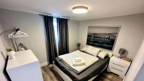 A modern bedroom with a bed, bedside tables, a desk, and a window with curtains.