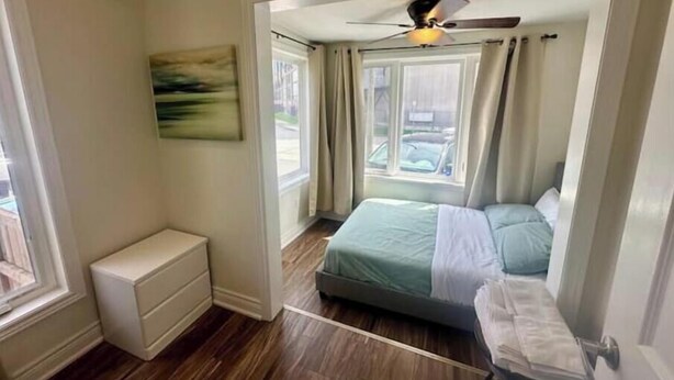 A bedroom with a bed, a nightstand, a dresser, a ceiling fan, and a window with curtains.