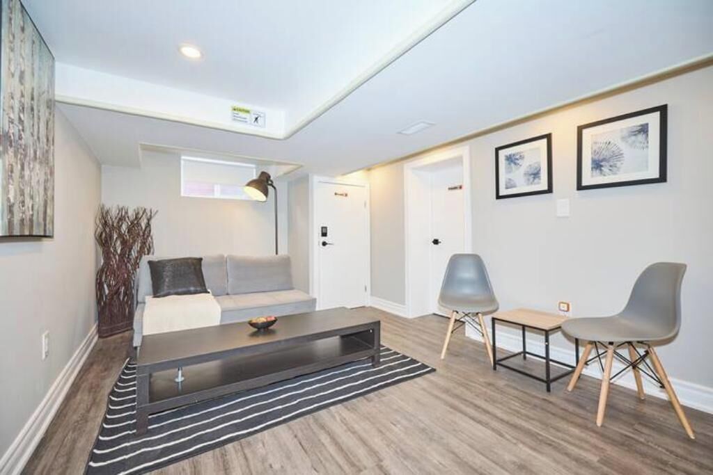Ein modernes Wohnzimmer mit einer Couch, einem Couchtisch und zwei Sesseln. Eine Tür und ein gerahmtes Bild sind an der Wand zu sehen.