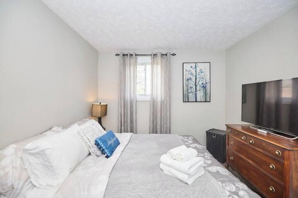 A hotel room with a bed, a TV, a dresser, and a window with curtains.