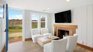 Una sala de estar moderna con chimenea, mobiliario blanco y ventanas amplias que ofrecen vistas al exterior.