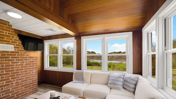 Un salón acogedor con pared de ladrillo, techo de madera y un amplio ventanal con vistas al exterior.