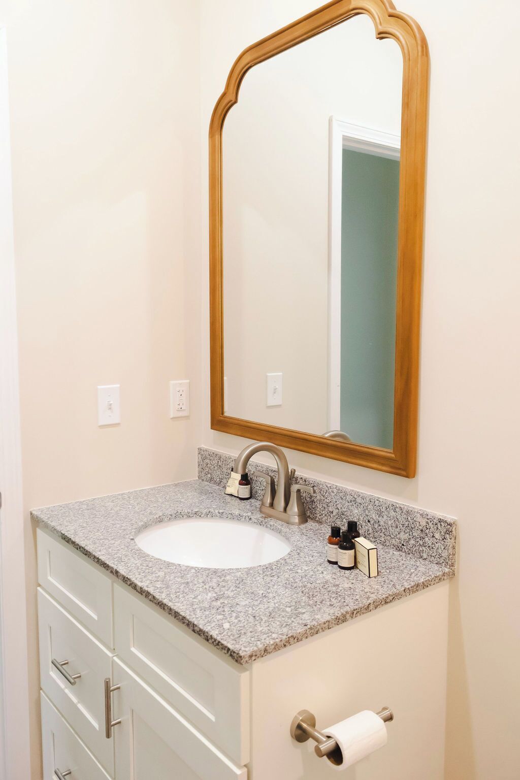 A bathroom with a granite countertop sink, a wooden-framed mirror, and a white cabinet with drawers.