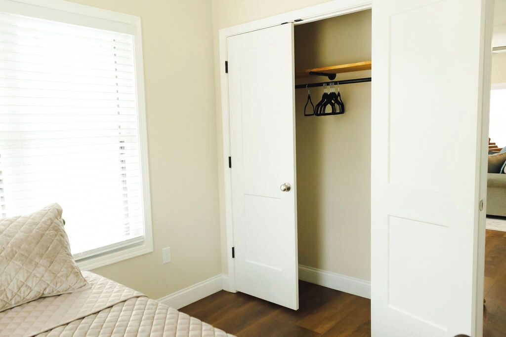 A bedroom with a bed, a window with blinds, a closet with a door open, and a wooden shelf.
