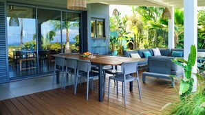 A modern outdoor dining area with a wooden table and chairs, a sofa, and a hanging light fixture. - Villa Acacias, Villa Acacias, piscine et vue panoramique (L'Étang-Salé)