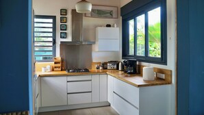A modern kitchen with white cabinets, a wooden countertop, a gas stove, and a window with a view of greenery. - Villa Acacias, Villa Acacias, piscine et vue panoramique (L'Étang-Salé)