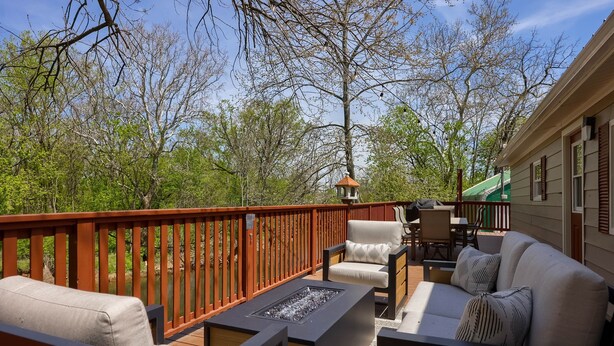 A deck with outdoor furniture, a fire pit, and a view of trees and a house. - Riverfront Stay |Deck, Views & Outdoor Living (Bird In Hand)