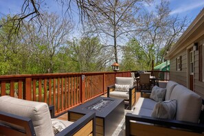 A deck with outdoor furniture, a fire pit, and a view of trees and a house. - Riverfront Stay |Deck, Views & Outdoor Living (Bird In Hand)