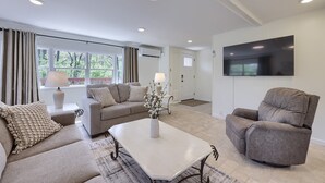 A modern living room with a beige sofa set, a white coffee table, and a large flat-screen TV mounted on the wall. - Riverfront Stay |Deck, Views & Outdoor Living (Bird In Hand)