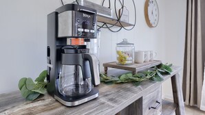 A coffee maker on a wooden table with a clock and a jar of cookies in the background. - Riverfront Stay |Deck, Views & Outdoor Living (Bird In Hand)